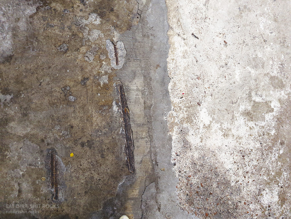 Lengths of rebar showing through a section of floor in a multi-level underground parking lot.