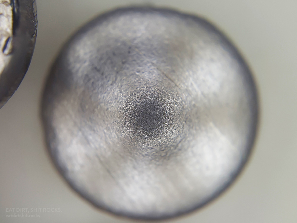 An 304 stainless steel metal confetto, viewed through a clip-on mobile phone 'microscope'. It's in convex orientation, with the central bulge facing towards the viewer (like a bowl resting upside-down.