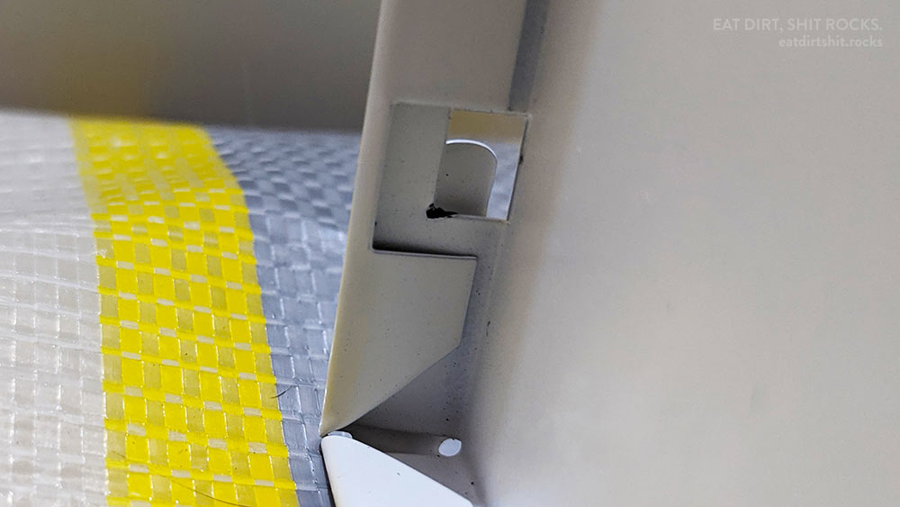 One of the four fold-over tabs that hold the back panel of each drawer in place, before folding but with the rear panel (mostly) in place.